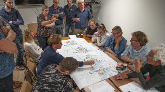 Inwoners van Woltersum zitten met een grote groep aan tafel, om een plattegrond van Woltersum heen, en praten over de dorpsvernieuwing van Woltersum.