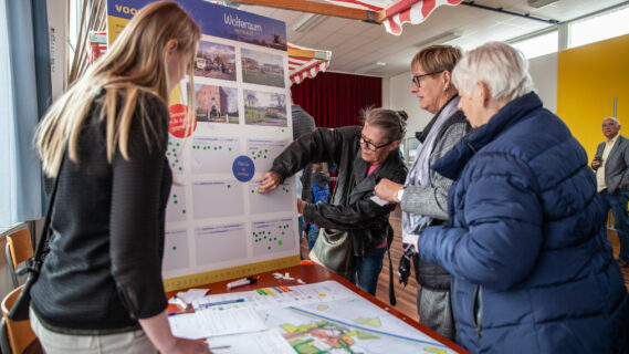 Inwoners staan bij een kraampje waar een mevrouw uitlegt wat haar plannen zijn voor de dorpsvernieuwing in Woltersum.