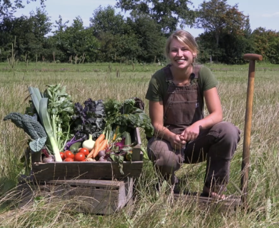 De drijfveer achter Tuinderij Het Groeipunt, Esther Kuiper, zit gehurkt naast een kratje met groenten.