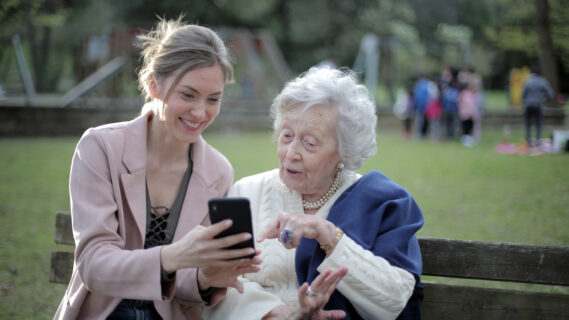 Decoratieve foto van een bejaarde vrouw en een vrouw van middelbare leeftijd die samen op een bankje naar een telefoon kijken