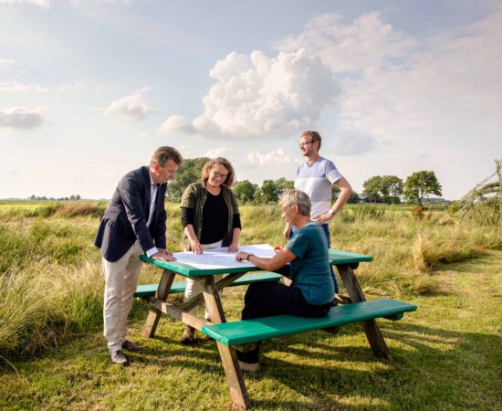Decoratieve afbeelding van initiatiefnemers van De Landschapswerkplaats om een picknicktafel, pratend over plannen