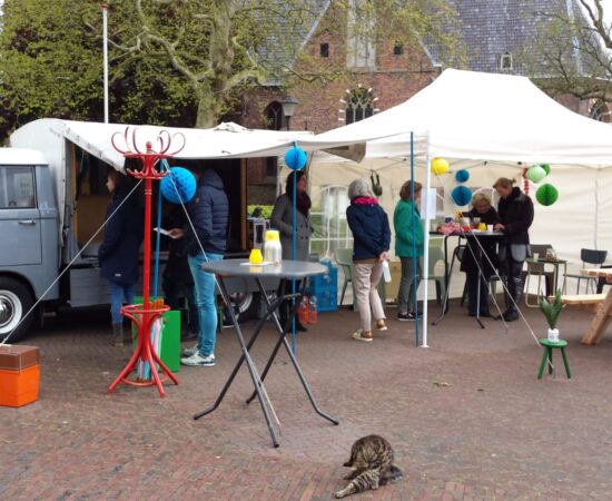 Foto van een busje en een markt waar mensen lopen om ideeën op te halen in Loppersum