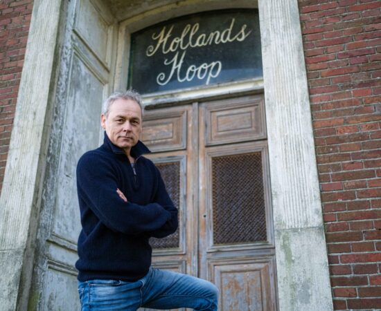 Marcel Hensema staat voor de boerderij waar de tekst "hollands hoop"boven een deur staat uitgebeeld