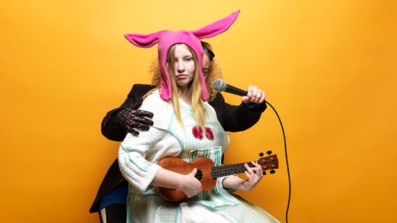 Decoratieve afbeelding van een meisje met een gitaar en konijnenoren met hierachter iemand met een microfoon